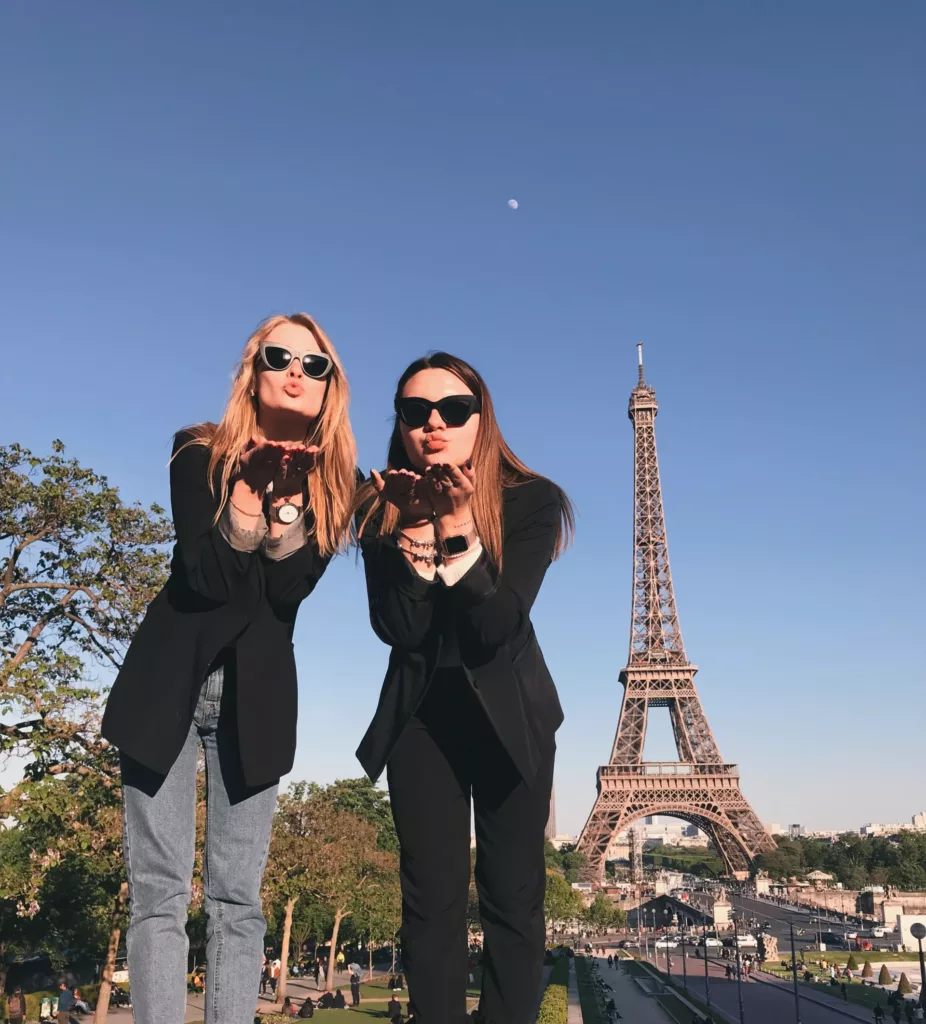 To unge kvinner med solbriller sender slengkyss foran høyt tårn