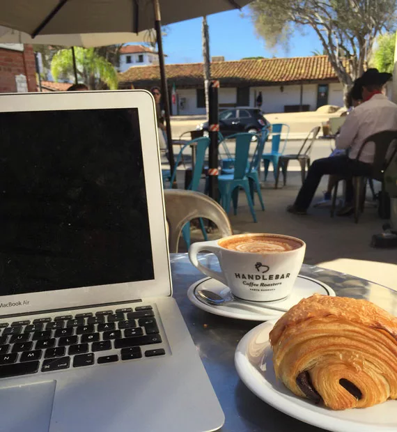 Bærbar Mac, kaffe og croissant på et cafébord i varmt strøk