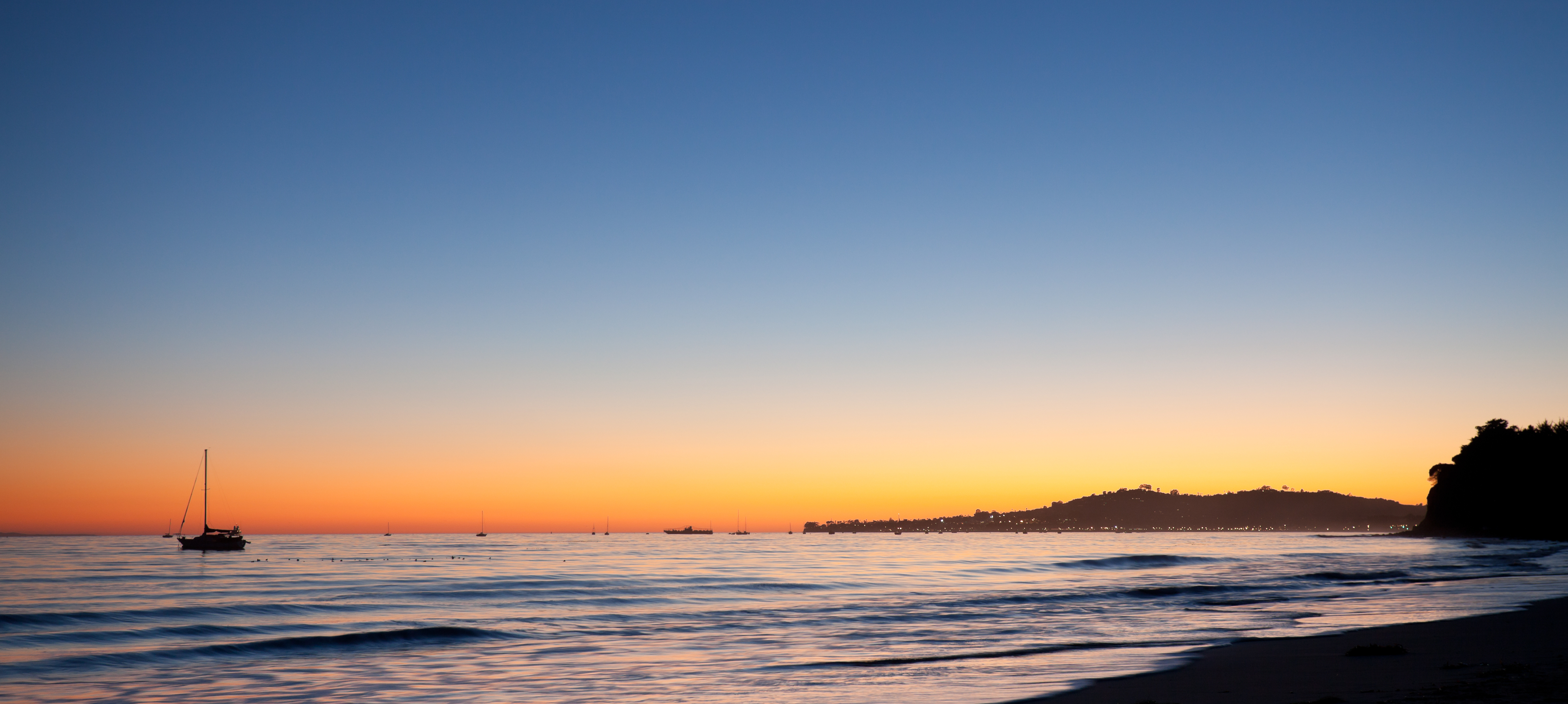 Solnedgang på en strand med seilbåt i horisonten