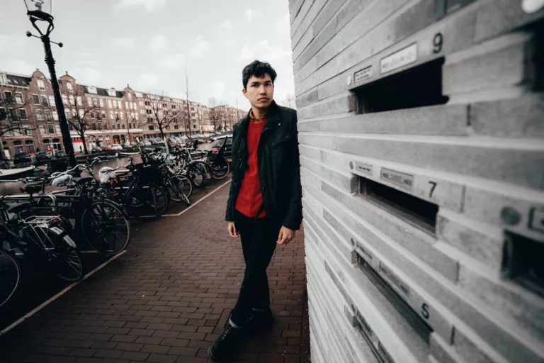Ung mann med rød skjorte står foran sykler i Amsterdam
