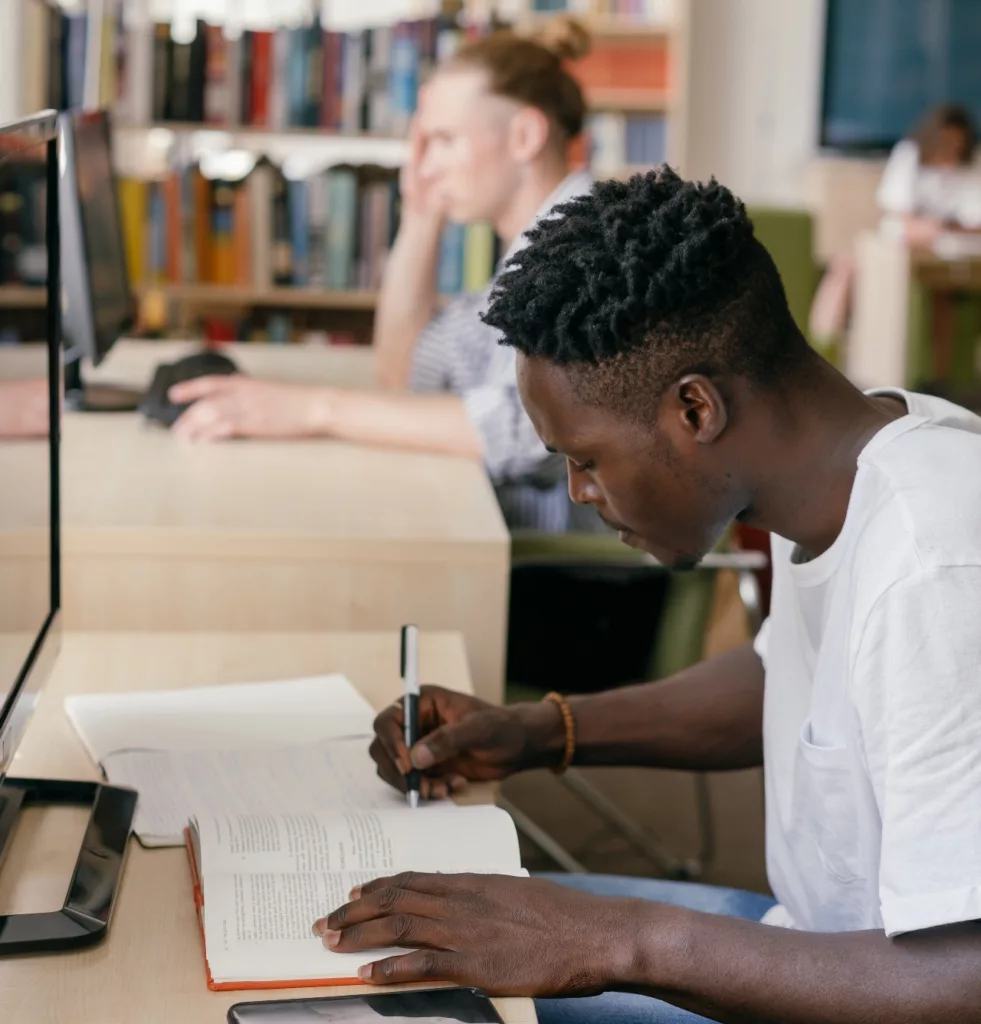 Ung mann sitter og leser og noterer i et bibliotek