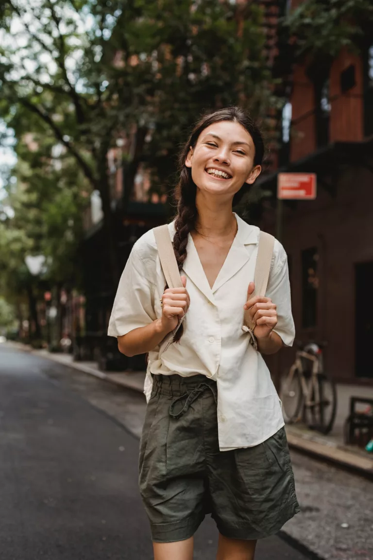 Ung kvinne med sekk smiler i en gate