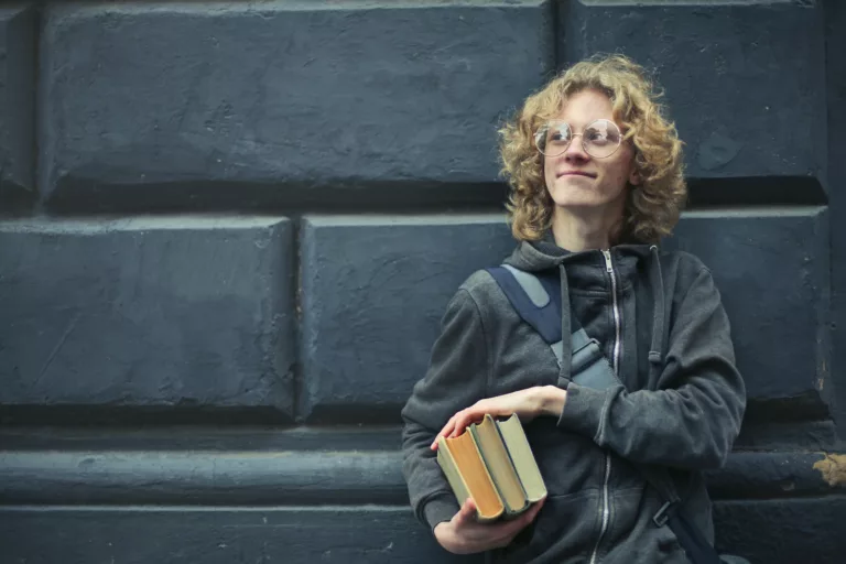 Ung mann med briller holder bøker i hendene
