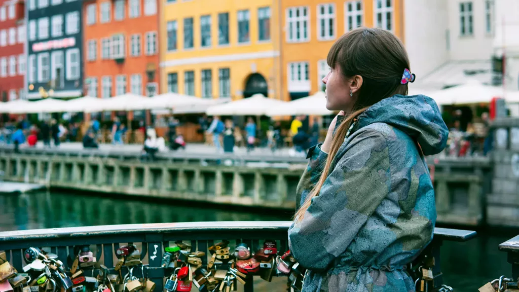 Ung kvinne står i regnjakke foran bygninger i København