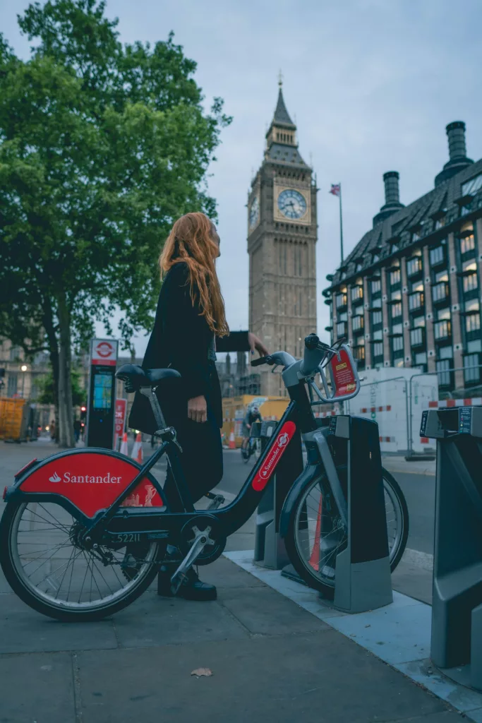 Kvinne med langt hår står med en sykkel foran landemerke i London