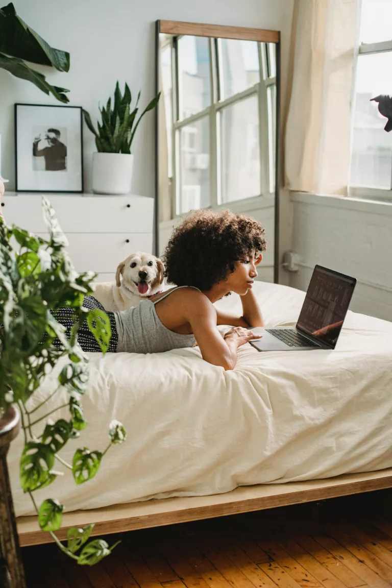 Kvinne med svart hår ligger i sengen med PC og hund