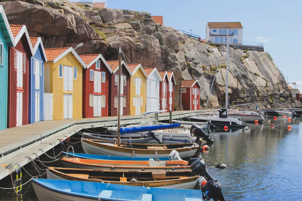 Båter som ligger til kai med fargerike båthus langs skjærgård