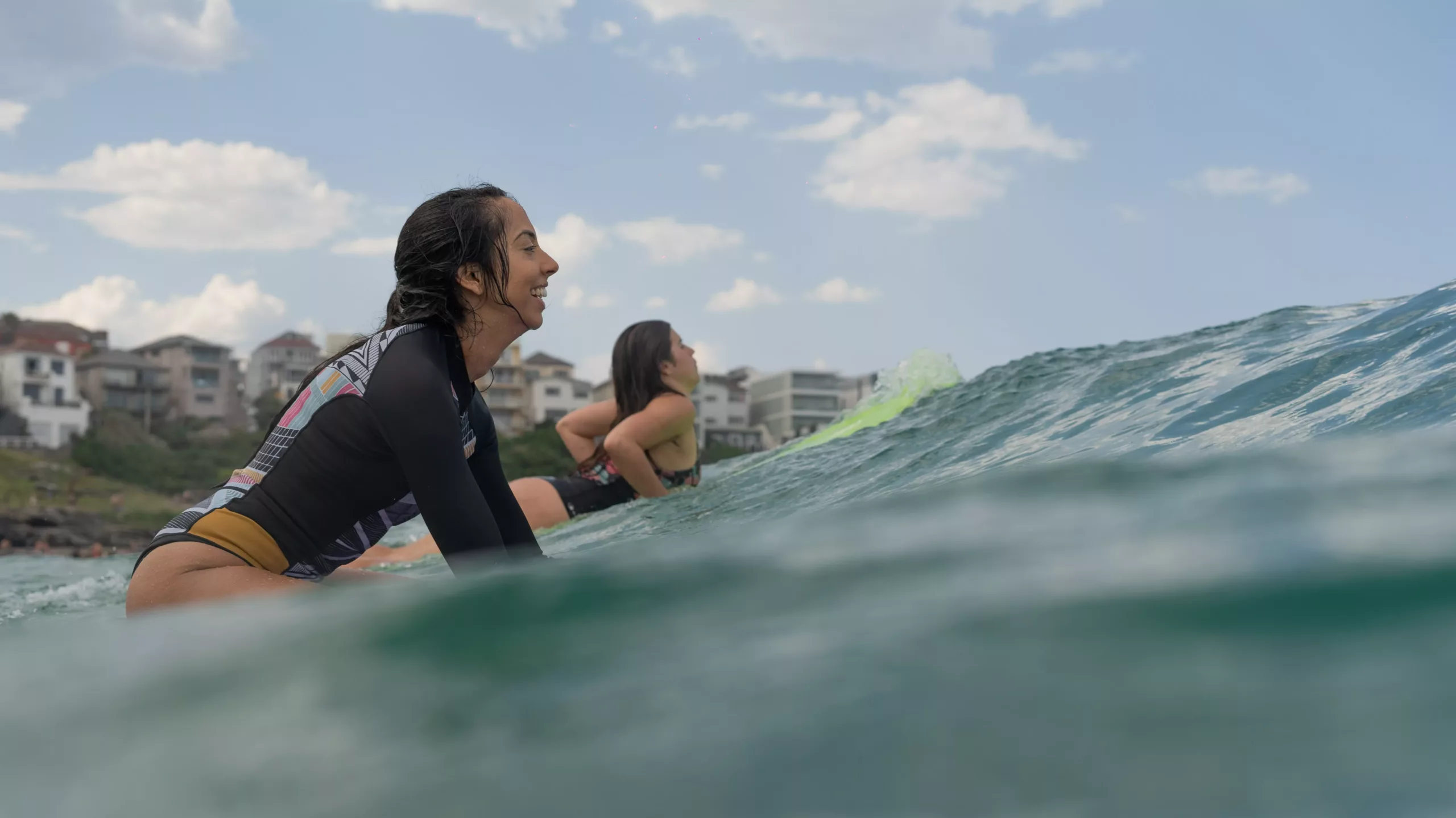 To kvinner ligger på surfebrett i vannet