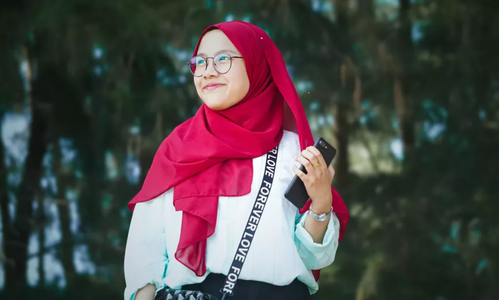 Ung kvinne med rød hijab holder en mobil