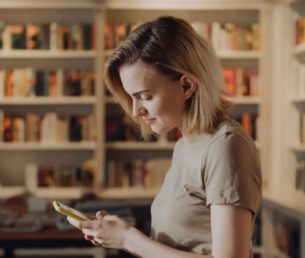 Ung kvinne i bokhandel leser på mobilen