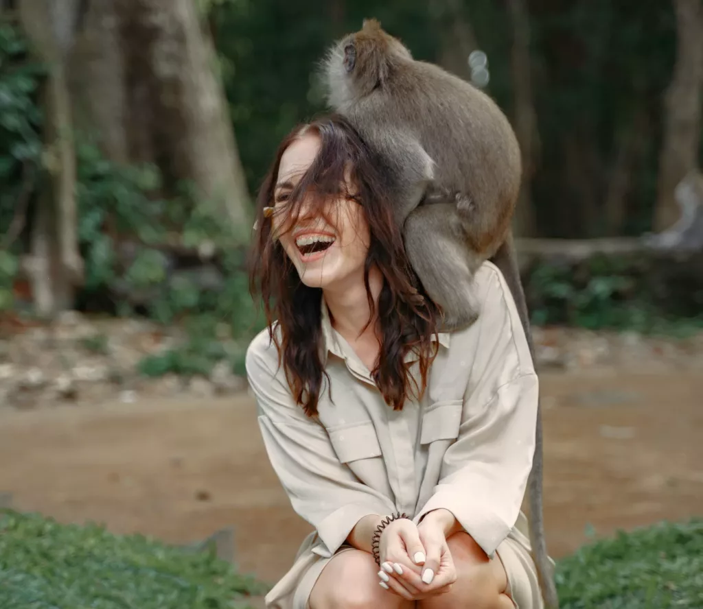 Ung kvinne ler med en grå ape på hodet