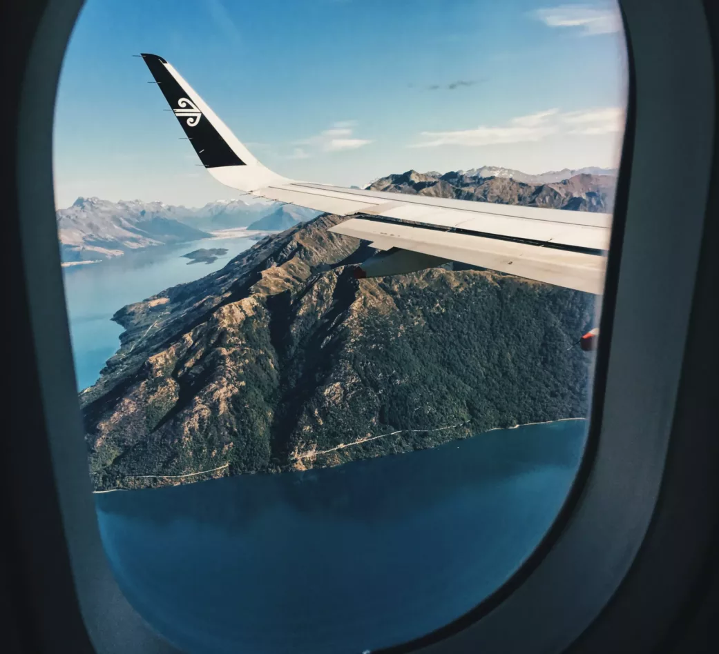 Utsikt fra flyvindu av flyvinge, sjø og fjell