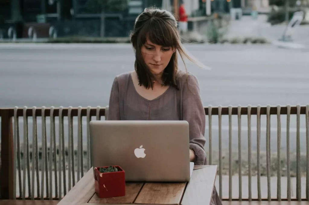 ung kvinne sitter ute på en kafé i en by og skriver på PC