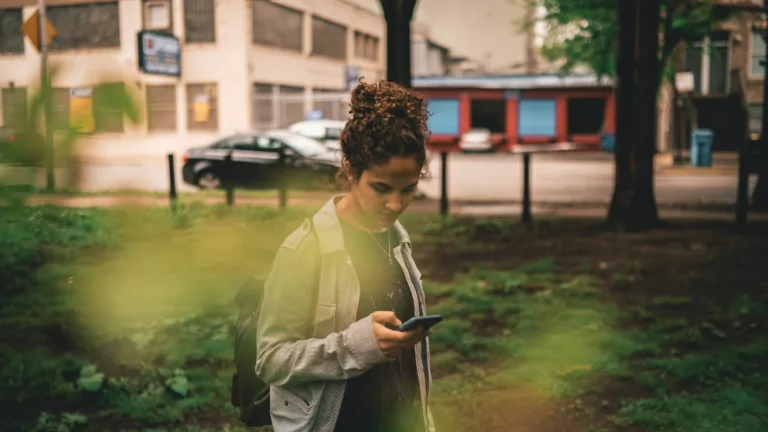 Kvinne bak blader ser på mobil i en park