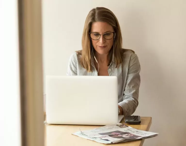 Kvinne med briller sitter ved et bord og jobber på PC