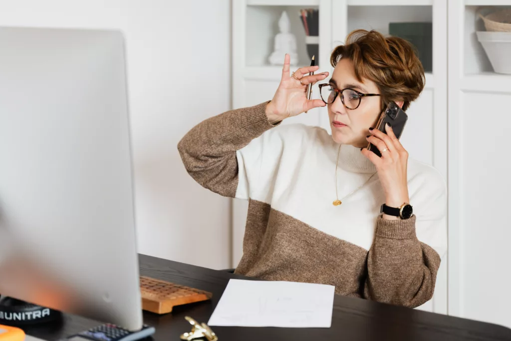 Kvinne med briller snakker i telefon ved en datamaskin