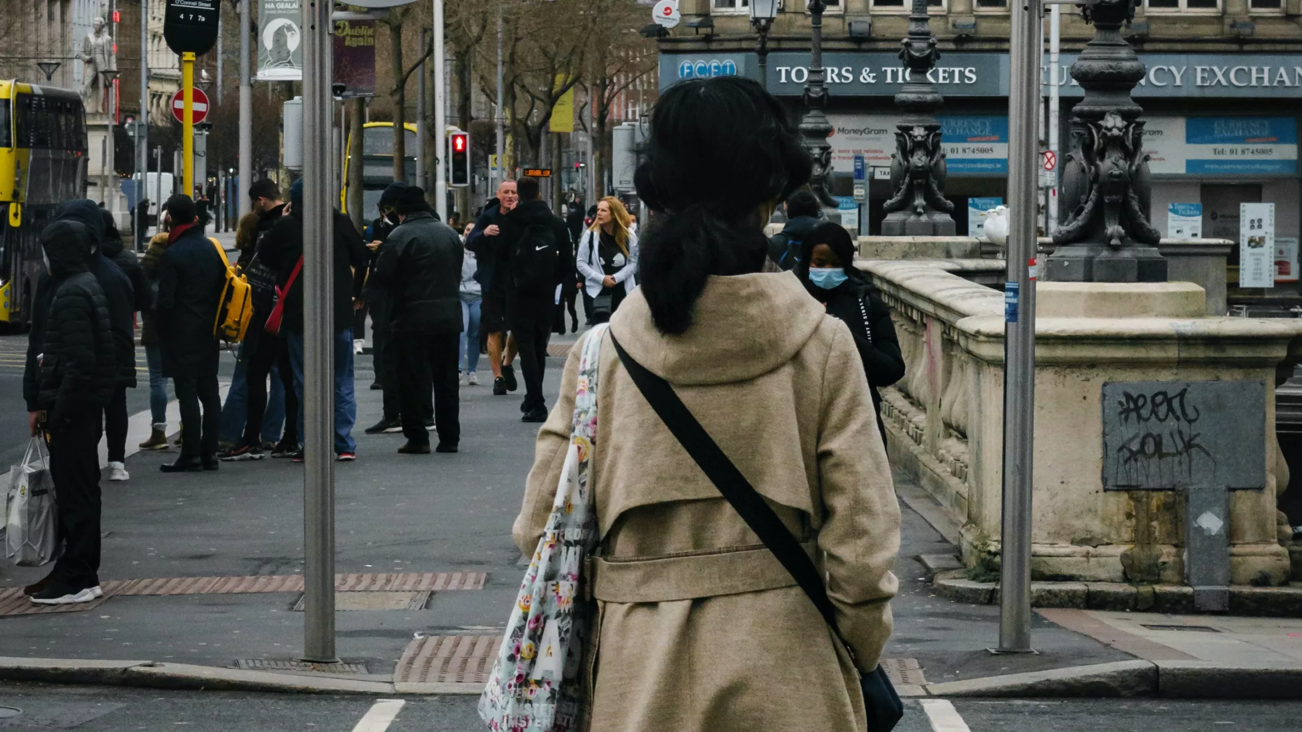 En ung kvinne i brun kåpe står foran en gate i Dublin, Irland