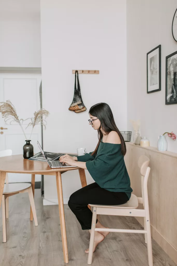 Kvinne med svart hår og briller sitter ved et bord og skiver på PC