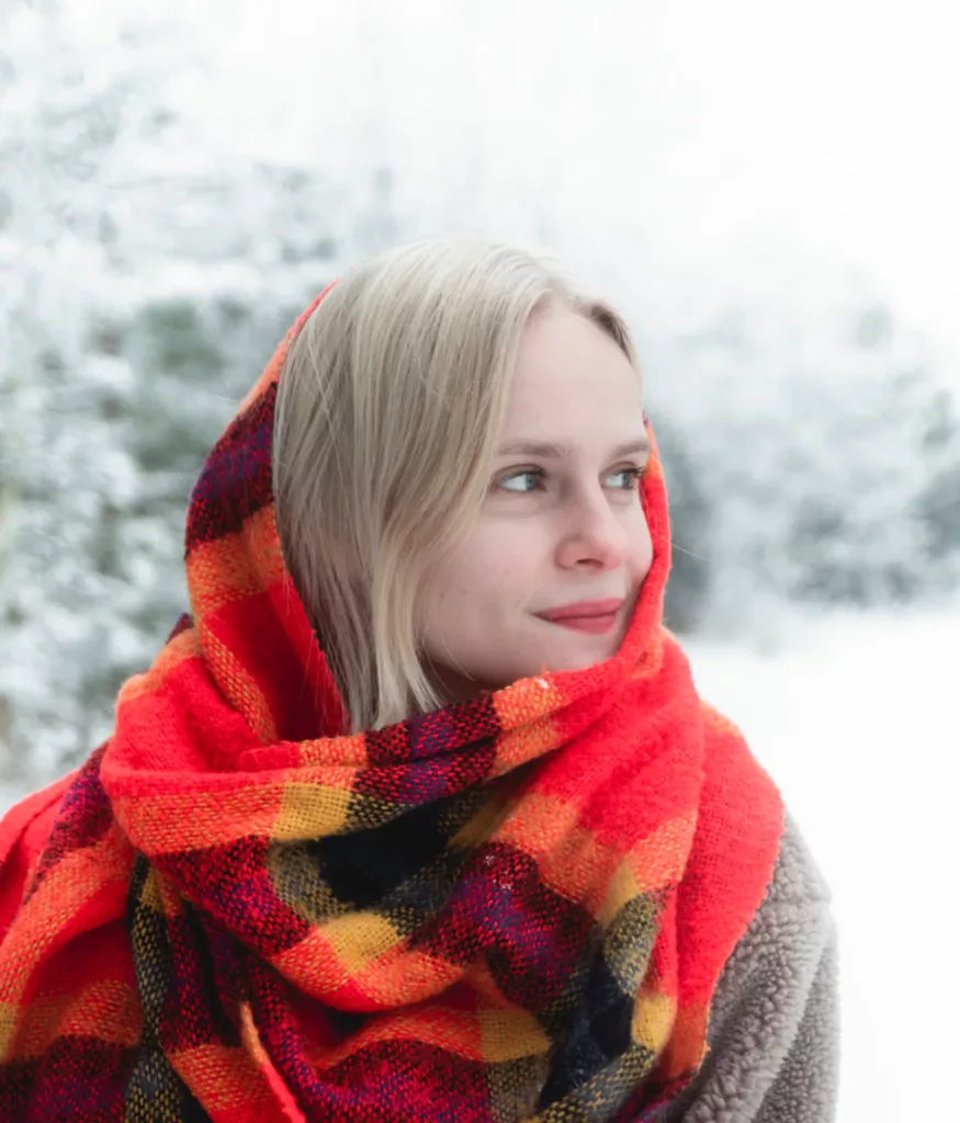 Ung kvinne med blondt hår og et rødt skjerf rundt hodet, står i landskap med snø