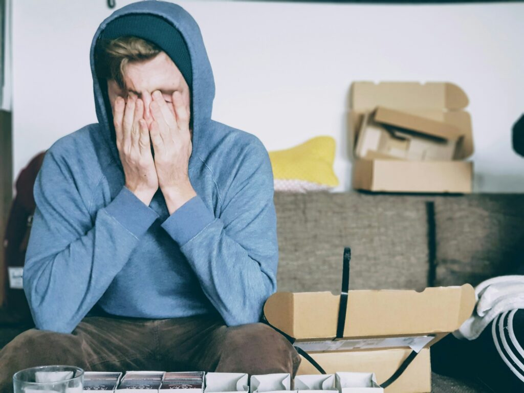 Mann dekker ansiktet med hendene mens han sitter i en sofa
