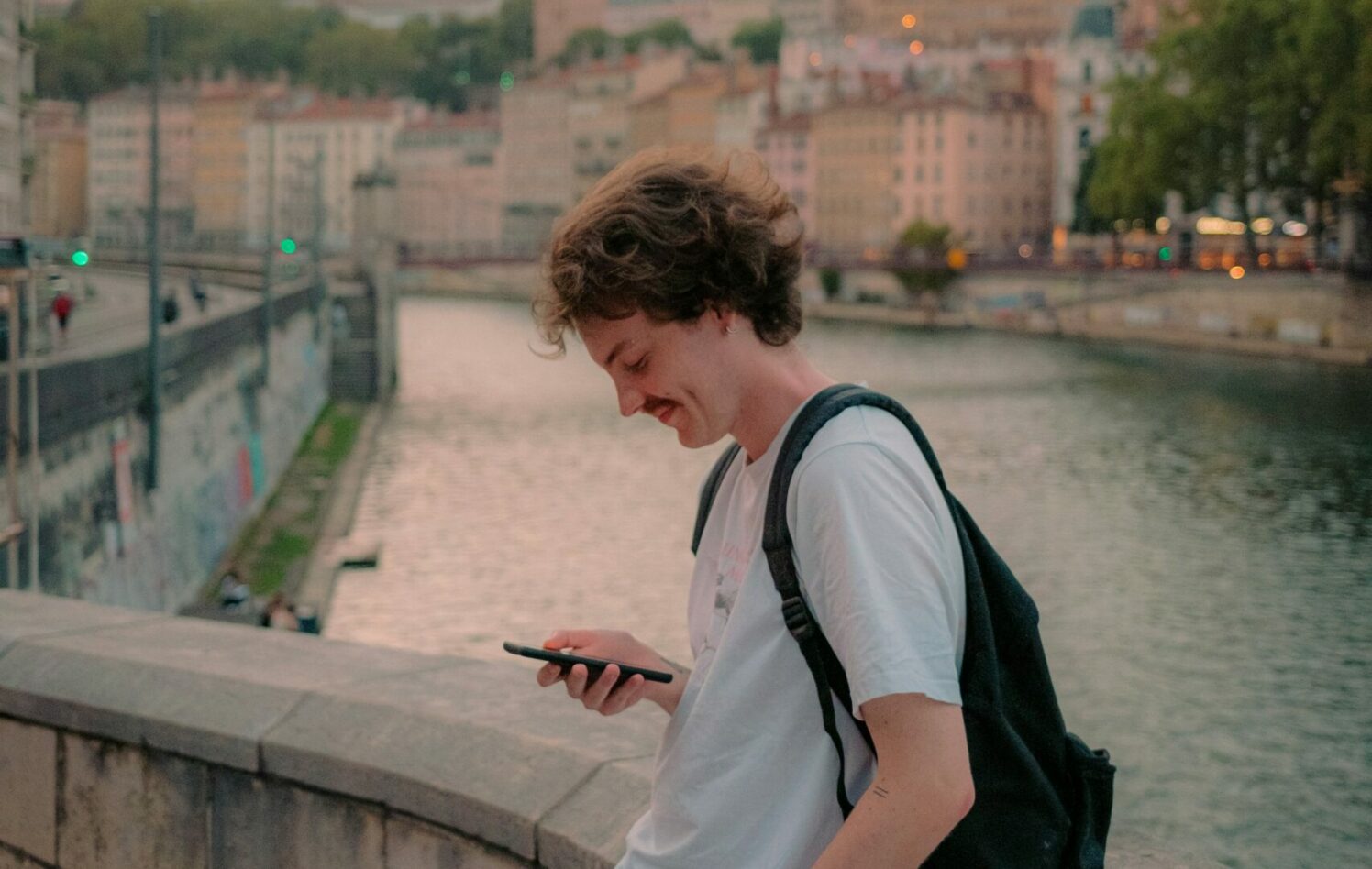 Ung mann sitter på en mur og ser på mobilen